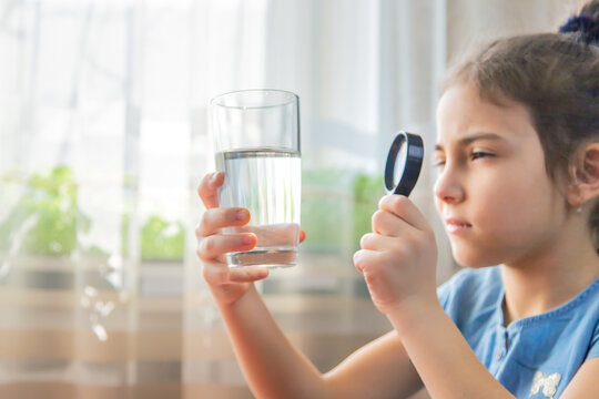 The child examines the water with a magnifying glass in a glass. Selective focus.