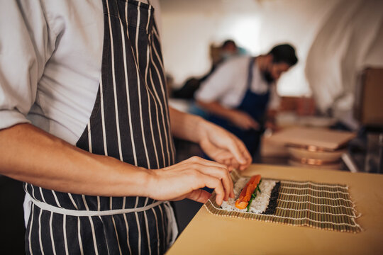 Close up shot of a professional sushi chef preparing salmon maki roll in a restaurant. Traditional Japanese omakase style. Concept of hospitality.