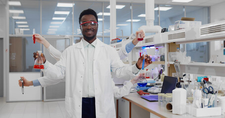 Multihanded afro laboratory scientist in lab coat and safety goggles holding flasks and test tubes