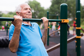 Fototapeta na wymiar mature cheerful pensioner man doing physical exercises on sports equipped playground