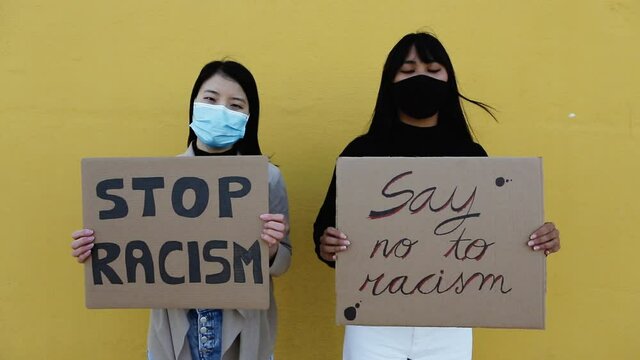 Asian young women protesting for equal rights while standing against a yellow wall during stop asian hate fight campaign
