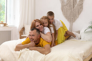 Portrait of beautiful young mother, father and their kids looking at camera and smiling while lying on bed leaning on each other