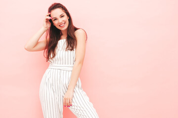 Portrait of young beautiful smiling female in trendy summer hipster overalls clothes. Sexy carefree woman posing near pink wall in studio. Positive model having fun indoors. Cheerful and happy