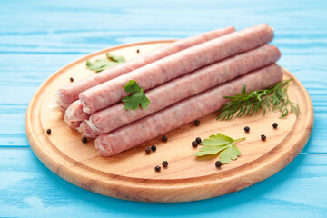 Raw sausage on cutting board on blue background. Top view