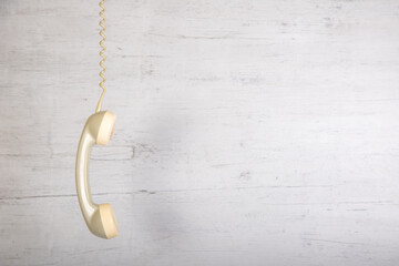 Fototapeta na wymiar Ein alter Telefonhörer hängt am Telefonkabel vor einem grauen Holzbrett und bietet Platz für Text
