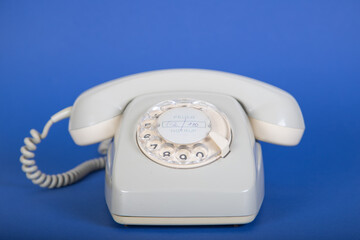 old grey telephone with dial plate, blue background