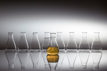 Scientific laboratory flask filled with yellow liquid with glassware equipment on reflective surface.
