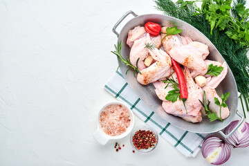 Raw chicken wings in a white bowl with spices and ingredients for cooking on light slate, stone or concrete background. Top view with copy space. Mock up.