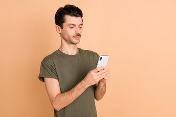Photo portrait of man keeping mobile phone using app reading news serious isolated on pastel beige color background