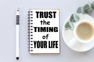 Trust The Timing Of Your Life. text on white notepad paper. near cups with coffee and plants on a gray background.