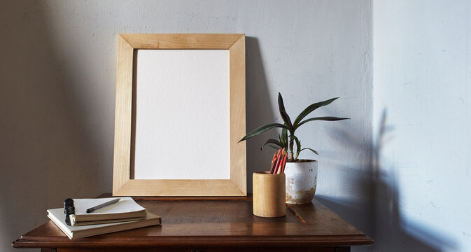 Wooden picture frame mockup. Flowerpot on a pile of books on an old wooden desk. Composition on a white wall background