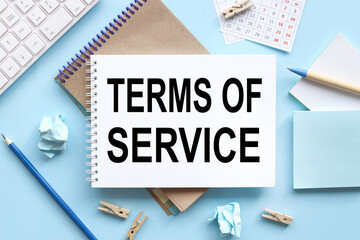 Term of service. text on white notepad paper on blue background. near the blue sticks and a white keyboard