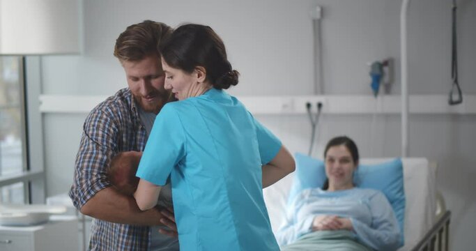 Nurse giving newborn son wrapped in blanket to young father in hospital