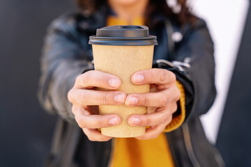 vertical view of unrecognizable woman drinking a recycled coffee cup outdoors. Disposable drinking container with hot coffee. Healthy caffeine drink concept.