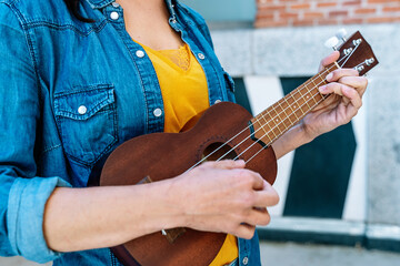 horizontal view of unrecognizable woman playing the ukelele outdoors. Entertainment, music and leisure concept on holidays.