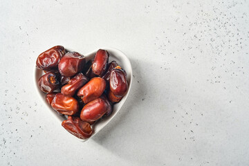 Dried sliced date fruit in a heart-shaped ceramic plate on white background with copy space. Snack vegan sugarfree food.