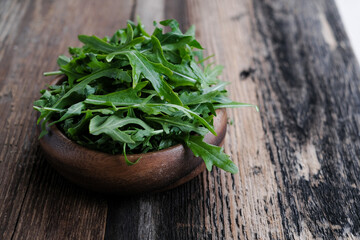 Arugula grass leaves in round wooden bowl at wooden table background