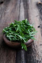 Arugula grass leaves in round wooden bowl at wooden table background