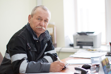Elderly employee at a table in the office.Foreman commander