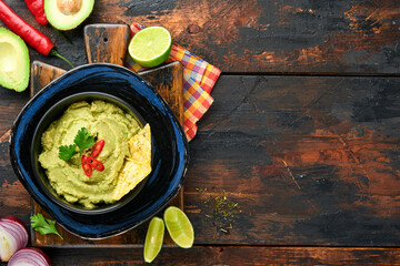 Guacamole. Traditional latinamerican Mexican dip sauce in a black bowl with avocado and ingredients and corn nachos. Avocado spread. Top view. Copyspace