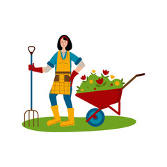 A young girl with a pitchfork stands next to a wheelbarrow with seedlings of flowers. A hobby is gardening.