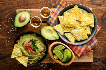 Guacamole. Traditional latinamerican Mexican dip sauce in a black bowl with avocado and ingredients and corn nachos. Avocado spread. Top view. Copyspace