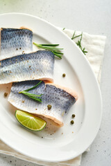 Salted herring with spice, herbs and onion on white plate on light stone background with copy space. Marinated sliced fish. Food with healthy unsaturated fats, flat lay