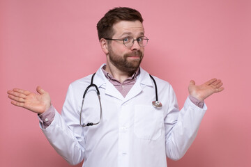 Surprised doctor with a stethoscope around neck innocently spreads hands and looks at the camera. Pink background.