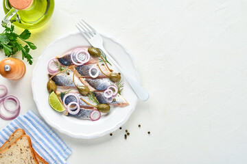 Salted herring with spice, herbs and onion on white plate on light stone background with copy space. Marinated sliced fish. Food with healthy unsaturated fats, flat lay