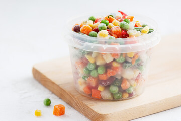 Mix of frozen vegetables in a container on a wooden board.