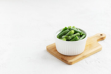 Frozen green beans in a bowl on a wooden board. Horizontal orientation, copy space.