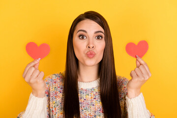 Photo of charming flirty young woman hold hands small heart shapes send air kiss isolated on shine yellow color background