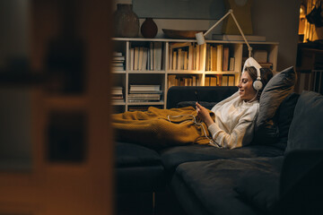 young woman listening to a music on headset. she is relaxing on sofa at her living room. evening...