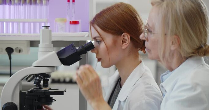 Team of scientists working together conduct experiment and look on microscope in modern laboratory