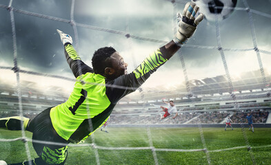 African male soccer or football player, goalkeeper in action at stadium. Young man catching ball,...