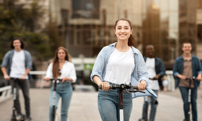 Woman having ride on motorized kick scooter with friends
