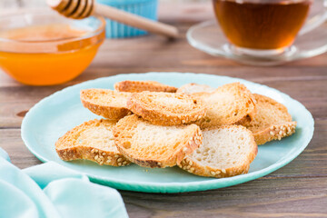 Small baguette toast on a plate on a wooden table. Tea and honey for breakfast