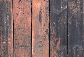 Old wall with vertical wooden planks with burgundy paint faded in the sun.