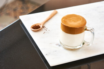 Dalgona coffee, fluffy creamy shake coffee in a transparent glass on a marble background next to a wooden spoon