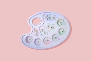 White palette with spots of paint and white spring flowers in it.