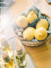 A few lemons in a wicker basket of rosemary. The basket sits on a wooden table.