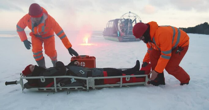 Lifeguards carrying victim on stretcher and loading in hovercraft on frozen lake