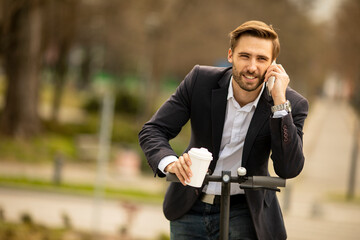 Young businessman using mobile phone while holding take away coffee cup on electric scooter