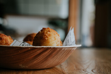 Side view of deep fried cheese ball on wood bowl