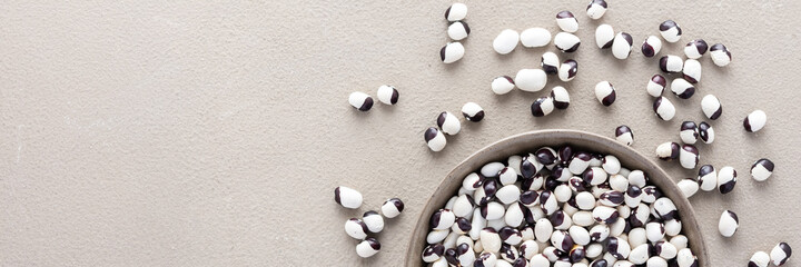 Legumes in bowl and scattered in the background, white and purple beans in a plate banner, top view, copy space