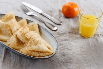 Breakfast with crepes or pancakes and jam, juice and tangerine on greige linen tablecloth. Pancake week or Shrovetide. Selective focus