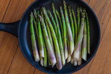Fried green asparagus in black pan on wooden background. Top view