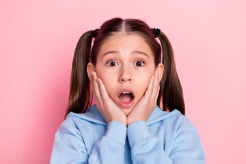 Photo portrait of surprised schoolgirl staring opened mouth touching cheeks isolated on pastel pink...