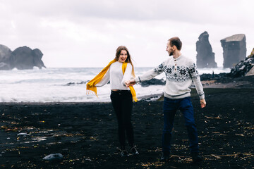 Icelandic tourist couple walking to the black sand beach south coast. Happy woman and man visiting tourist attraction.