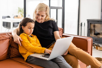 Working from home office with kid. Happy mother and daughter shopping online, using laptop together. Woman hugging child. Freelancer workplace. Female business, virtual communication.